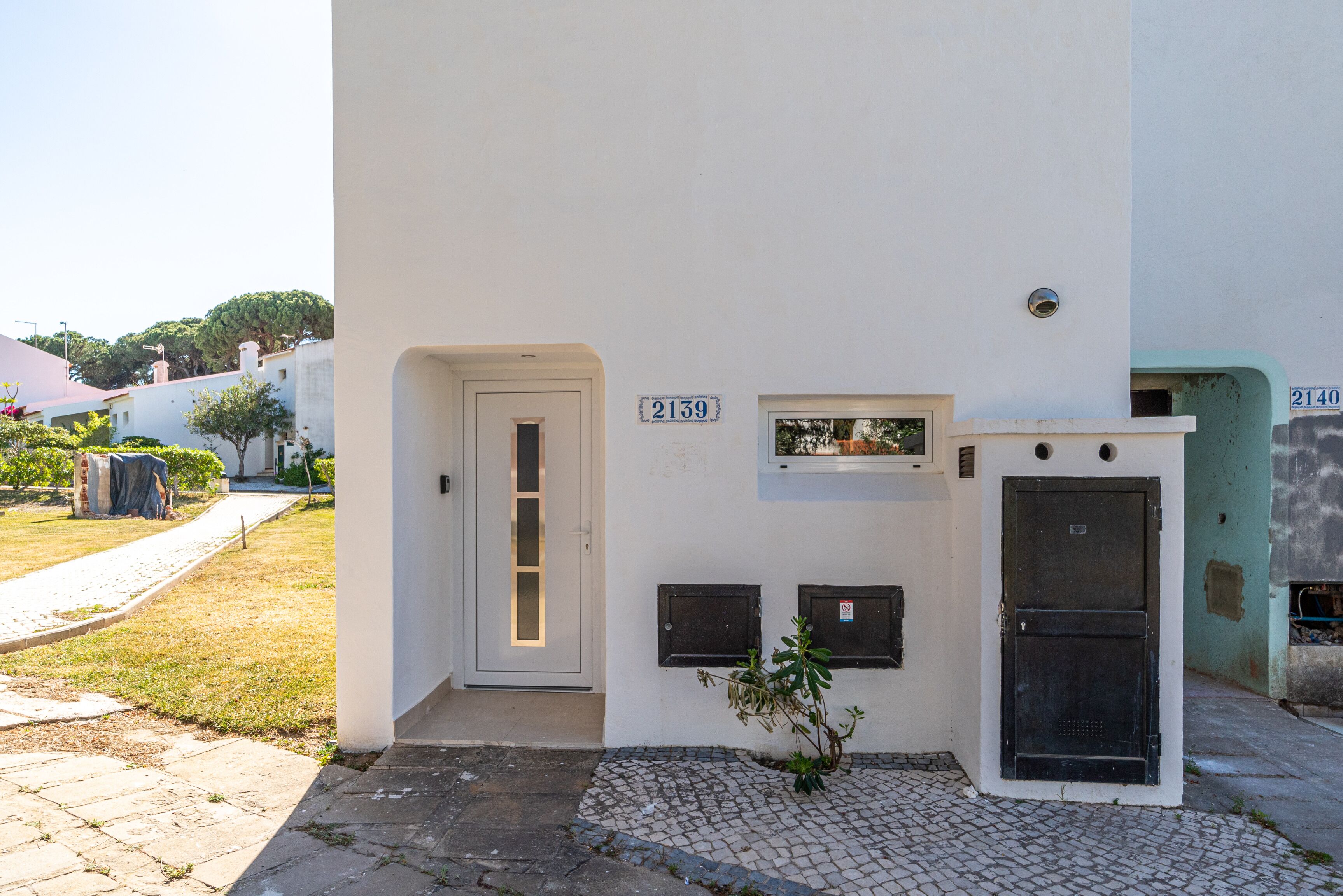 Ein Gebäude mit weißer Fassade, mit den Hausnummern 2139 und 2140, das eine Tür, kleine Fenster und einen Briefkasten zeigt.