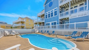 A pool area with lounge chairs and a building with balconies. - Oceanview Home in Avon w/ Pool, Hot Tub, EV Charger, and Community Beach Access (Avon)