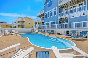 A pool area with lounge chairs and a building with balconies.