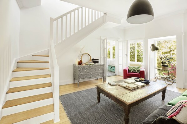 Un salón amplio con una escalera de madera, un ventanal grande y una zona de comedor con una mesa y sillas.
