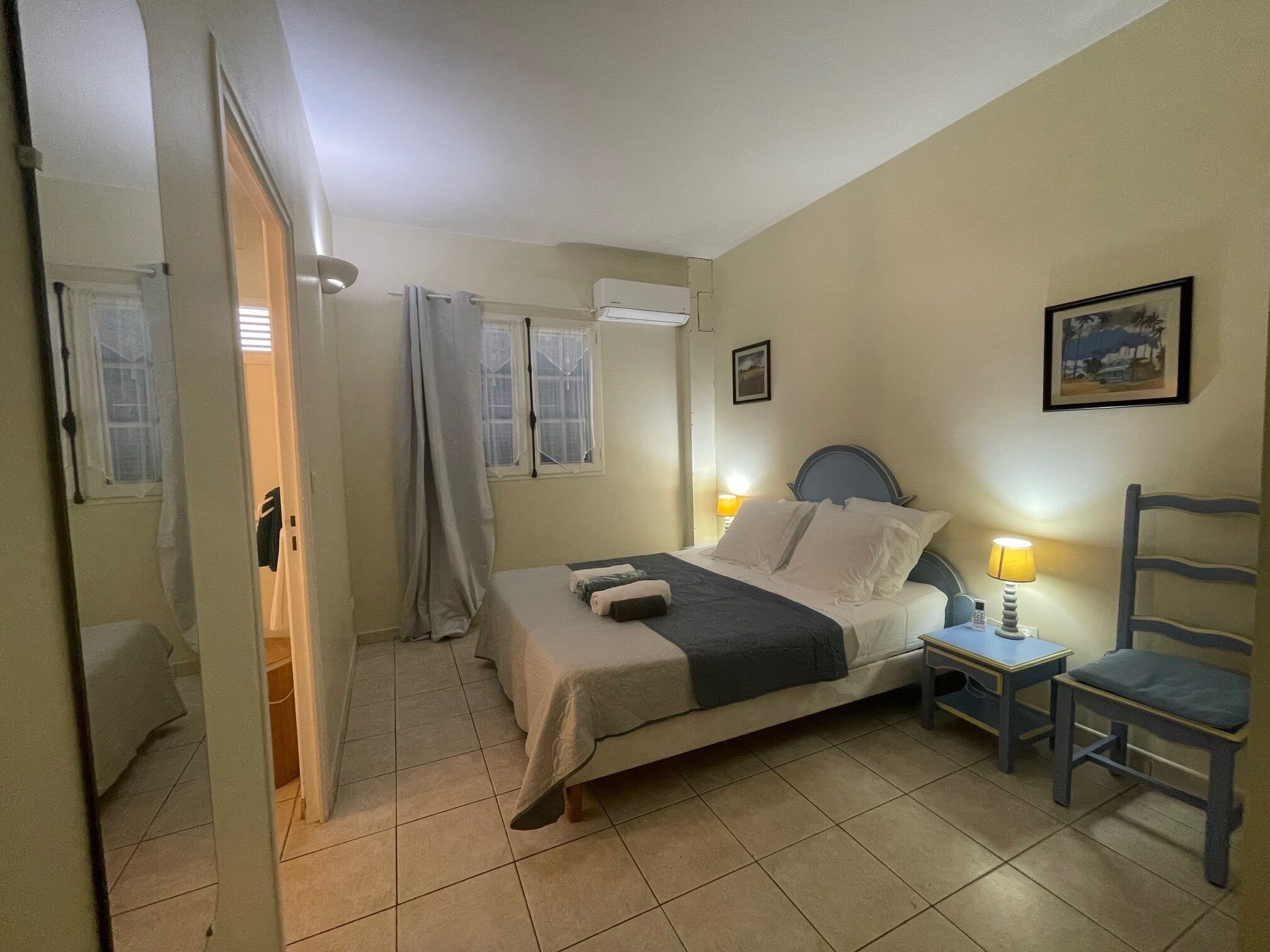 Une chambre à coucher avec un lit, une table de chevet avec une lampe, une chaise et une fenêtre.