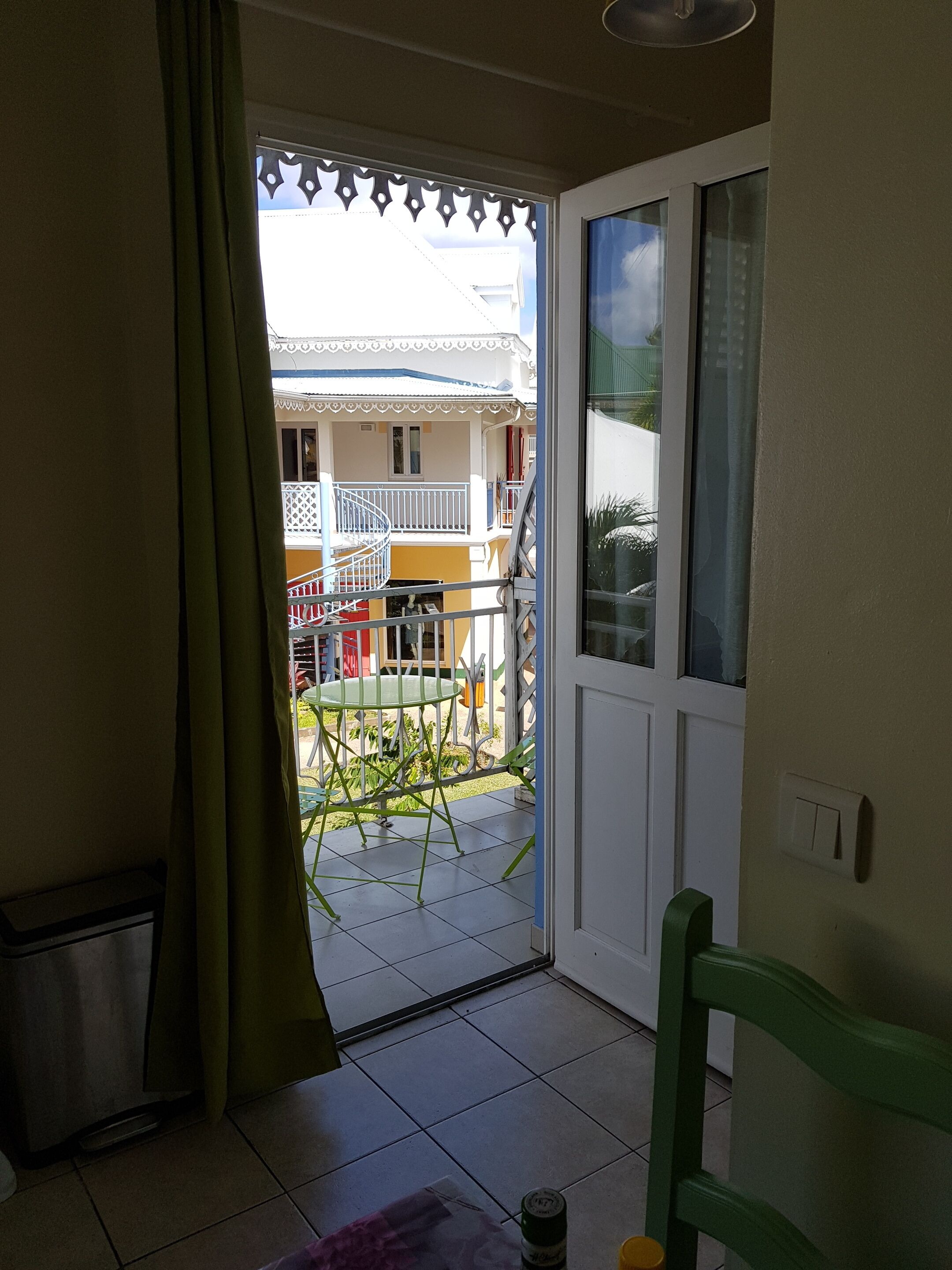 Quarto com porta de vidro deslizante que dá para uma varanda externa. A varanda possui guarda-corpo de metal e uma cadeira verde.