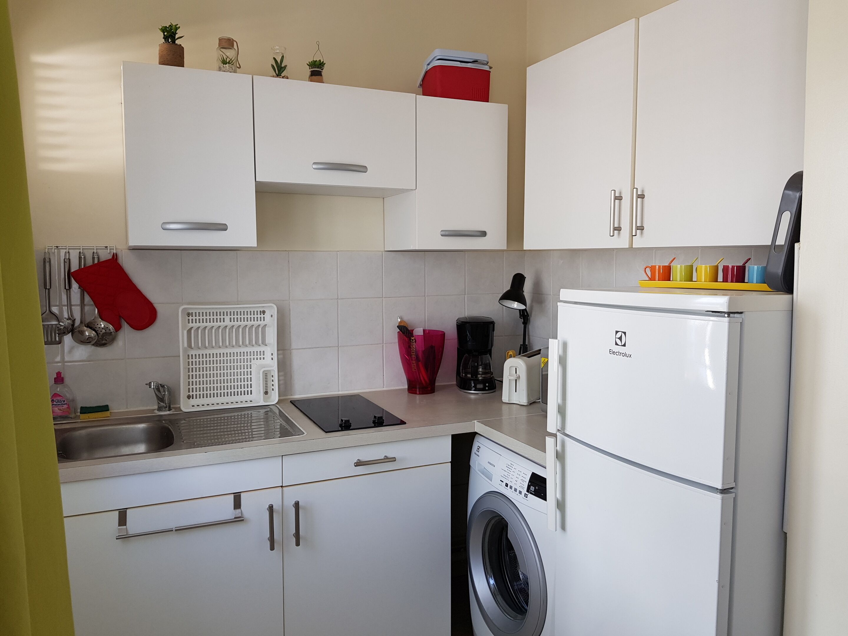 Una cocina compacta con lavadora integrada, cafetera y tostadora.