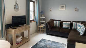 Sala de estar com televisão, móvel de TV de madeira, sofá e uma mesinha.