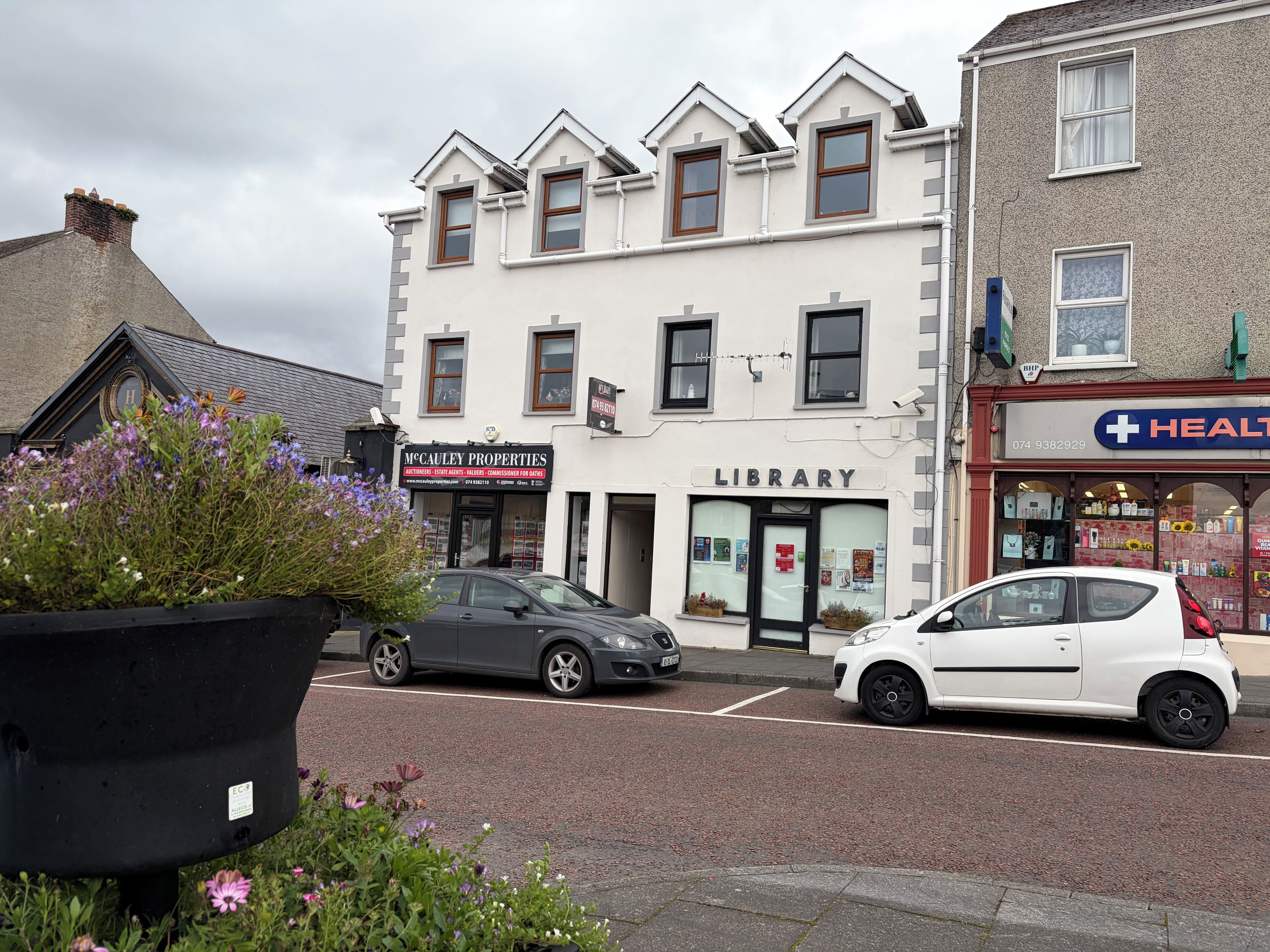 A street view with a library, a health store, and parked cars.