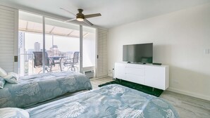 Habitación de hotel con dos camas, televisor, ventilador de techo y balcón con mesa y sillas.