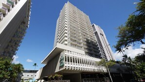 Un edificio alto y moderno con un diseño arquitectónico singular, que presenta una fachada inclinada y varios balcones.