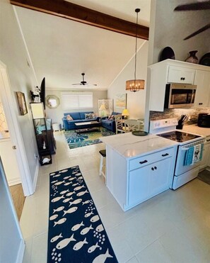 A modern kitchen with white cabinetry, a microwave, and a stove. There is a blue sofa in the living area and a patterned rug on the floor.