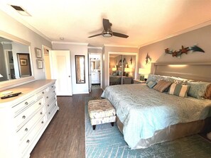 A bedroom with a large bed, a dresser, a mirror, a ceiling fan, and a walk-in closet.