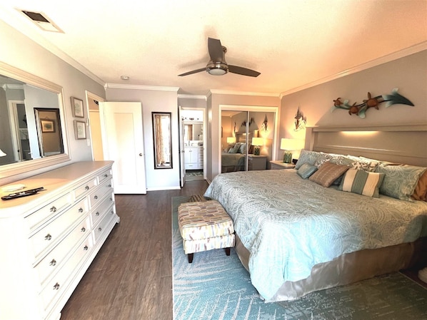 A bedroom with a large bed, a dresser, a mirror, a ceiling fan, and a walk-in closet.