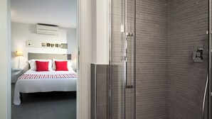 Een hotelkamer met een bed, een douchecel met een glazen deur en een wandgemonteerde airconditioning.