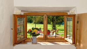 A bay window with a wooden frame, a vase with flowers, and a view of a garden and outdoor dining area.