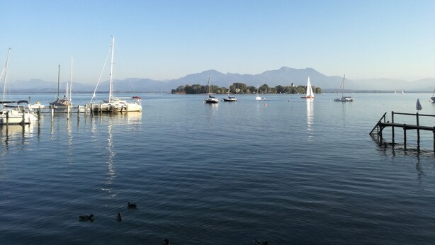 A marina with boats docked, calm water, and mountains in the background.