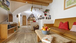 A cozy living room with a wooden bench, a bowl of fruit, and a book on the bench. There is a wooden cabinet and a television on a stand.