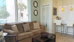 A living room with a sofa, a coffee table, and a dining area with a white table and chairs. - Destin West Villa 301, oceanview, wraparound balcony, lazy river, 6 pools, beach (Fort Walton Beach)