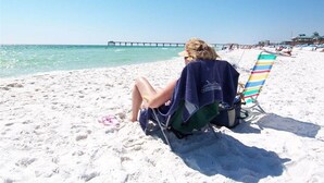 A beach scene with a person sitting on a beach chair, a pier in the background, and a clear sky. - Destin West Villa 301, oceanview, wraparound balcony, lazy river, 6 pools, beach (Fort Walton Beach)