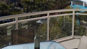 A glass-top table with four white plates, two wine glasses, and a water bottle on a balcony overlooking a pool and buildings. - Destin West Villa 301, oceanview, wraparound balcony, lazy river, 6 pools, beach (Fort Walton Beach)