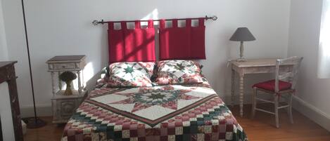 Quarto com uma cama grande, mesa de cabeceira, uma cadeira, abajur e um quadro na parede.