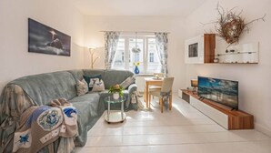 Ein Wohnzimmer mit einer Couch, einem Glastisch, einem Fernseher und einem Essbereich mit Tisch und Stühlen.
