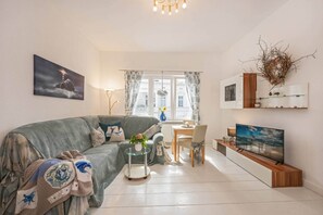 A living room with a sofa, a glass coffee table, a TV, and a dining area with a table and chairs.