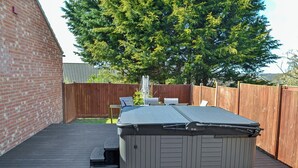 Un jacuzzi en una terraza de madera con un muro de ladrillo y una cerca de madera al fondo.
