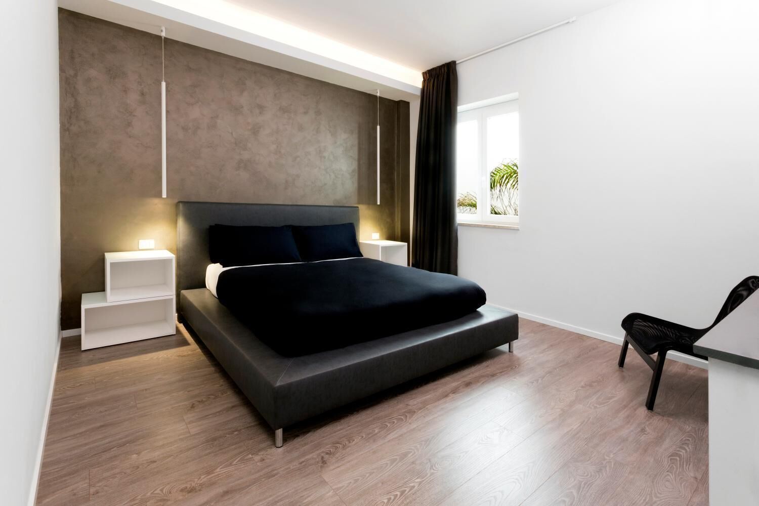A modern bedroom with a large bed, bedside tables, a window with curtains, and a chair.