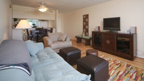 Ein Wohnzimmer mit einer Couch, Hocker, Fernseher und Schrank.