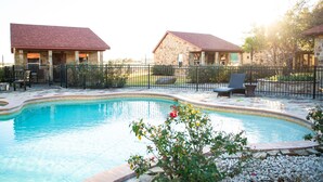 Ein Swimmingpool mit Steingrenze, umgeben von einem Zaun und zwei Gebäuden mit roten Dächern.