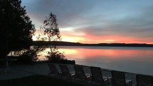 Vista de un lago al atardecer, con una fila de sillas y un árbol.