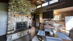 Un interior rústico con chimenea de piedra, vigas de madera en el techo y una zona de cocina con taburetes de bar.