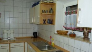 Une cuisine avec des murs recouverts de carreaux blancs, des meubles en bois, un évier à deux bacs et une cuisinière.