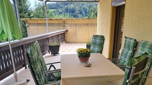 Une terrasse avec une table et des chaises, un pot de fleurs et une vue sur la forêt.