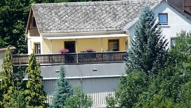 Une maison à deux étages avec un balcon, entourée d’arbres.