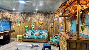 Et værelse med tropisk tema, der inkluderer en sofa med blomsterpuder, et lille bord med drikkevarer og en væg dekoreret med strandtema-effekter.
