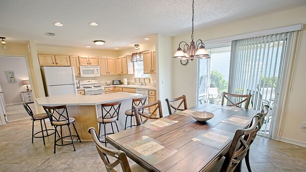 Una cocina amplia con armarios de madera, una isla central y una zona de comedor con una gran mesa y sillas de madera.