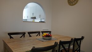 Een eetruimte met een houten tafel, zes stoelen, een fruitschaal, een spiegel en een wandklok.