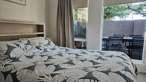 Een slaapkamer met een groot bed, een raam met gordijnen en uitzicht op buitenmeubilair.