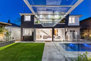Een modern huis met een glazen patio, een zwembad en een verzorgd gazon.