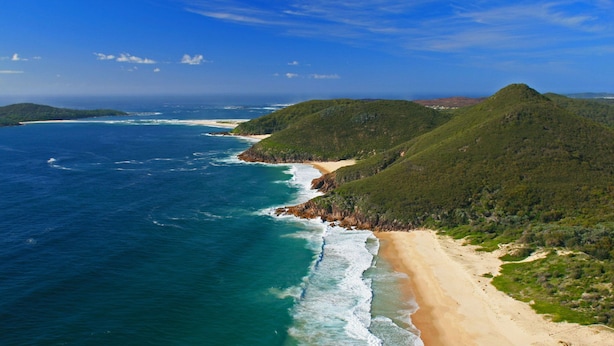 Un paysage côtier avec une plage, l’océan et des collines.