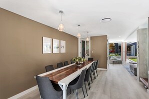 A modern dining area with a long wooden table, grey chairs, pendant lighting, and framed artwork on the wall. - La Luna Shoal Bay Luxury Holiday Home with Pool (Shoal Bay)