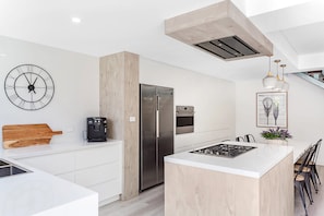 Een moderne keuken met een centraal eiland, roestvrijstalen apparatuur en een klok aan de muur.