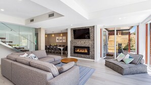 Un salon moderne avec un canapé gris, un plus petit canapé également gris, une table basse en bois et une cheminée dont le mur arrière est décoré de mosaïques.