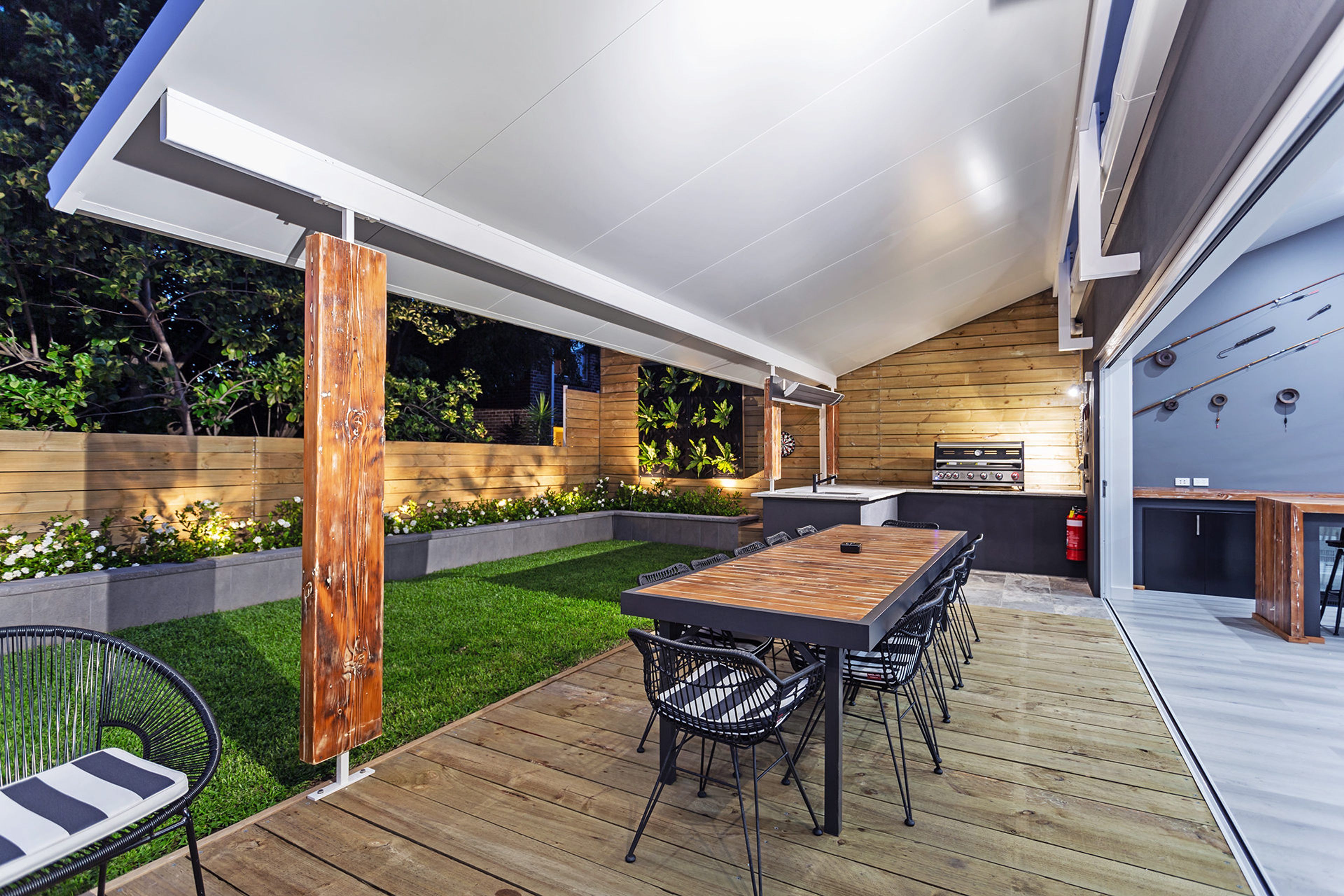 Een modern terras buiten met een houten terras, een eettafel met stoelen en een ingebouwde barbecue.