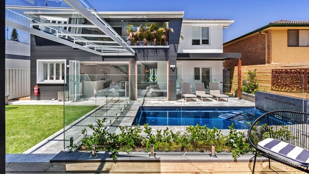 Une maison moderne à deux étages, dotée d’un patio entièrement vitré, d’une piscine et d’un jardin aménagé.