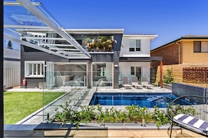 Une maison moderne à deux étages, dotée d’un patio entièrement vitré, d’une piscine et d’un jardin aménagé.