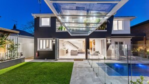 Une maison moderne à deux étages, dotée d’un patio entièrement vitré, d’une piscine et d’une pelouse bien entretenue.