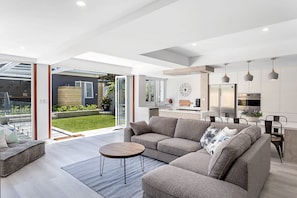 Un salon moderne avec un canapé d’angle, une table basse et une vue sur le jardin à travers des portes vitrées.
