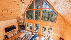 Una cabaña de madera espaciosa con una chimenea grande, una zona de estar acogedora y ventanas amplias que ofrecen vistas del bosque circundante.