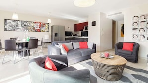 A modern living room with a grey sofa, a round coffee table, and a dining area with a table and chairs.