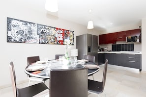 A modern dining area with a round table, chairs, and a large abstract painting on the wall.